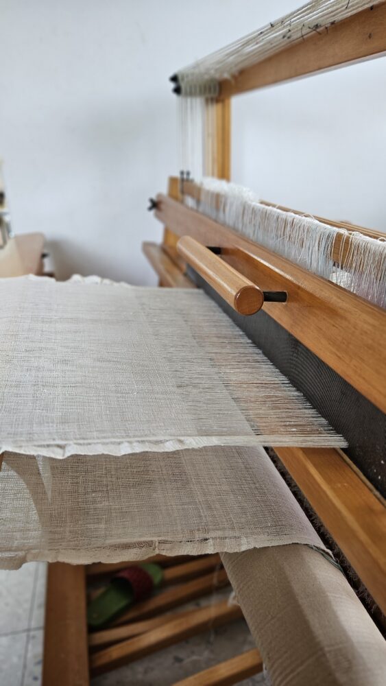 thin historical linen fabric on loom. Fabric has frilled decorative edges.